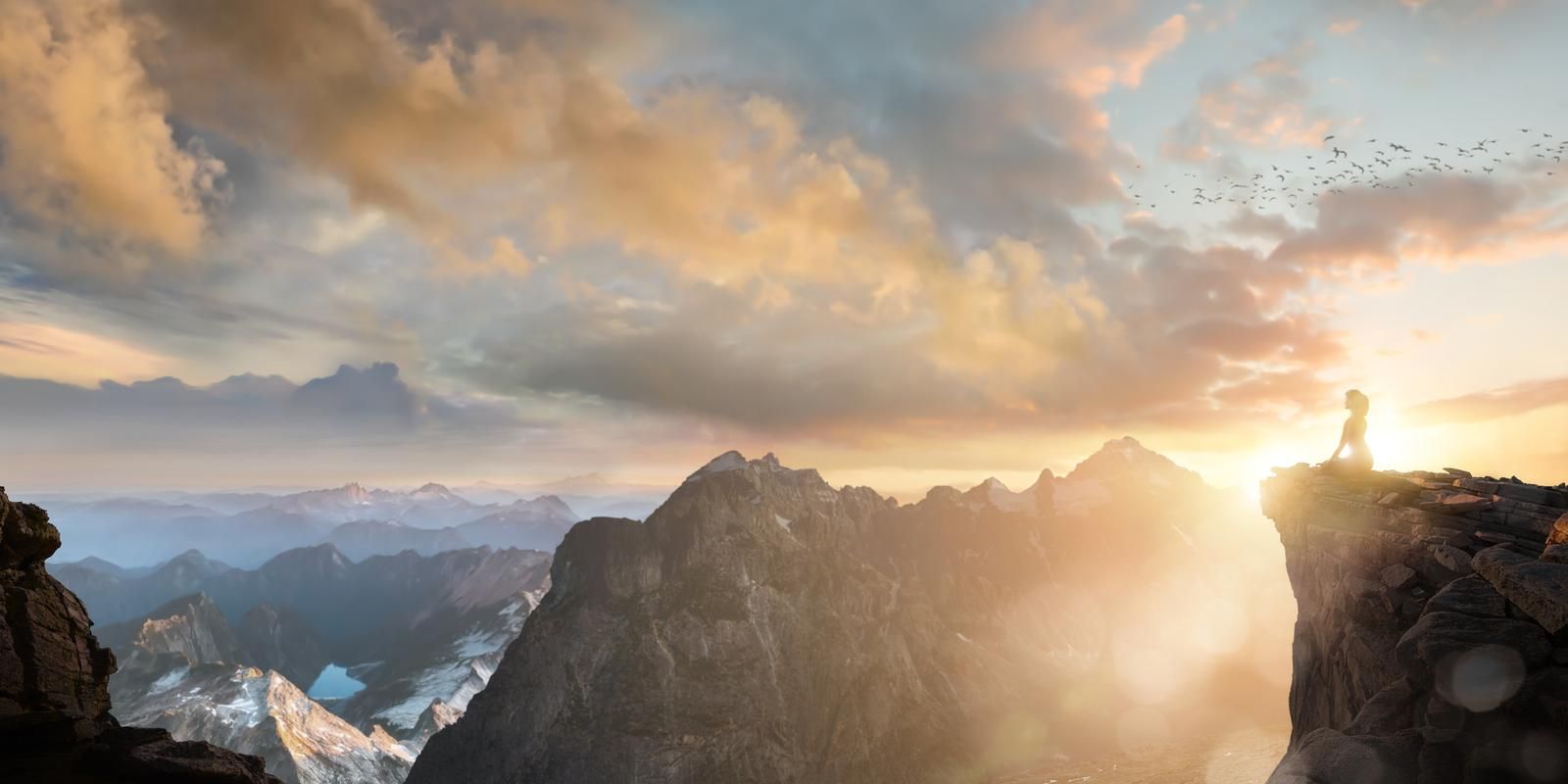 Meditierende Person auf einem Felsvorsprung über Berggipfeln im Sonnenaufgang
