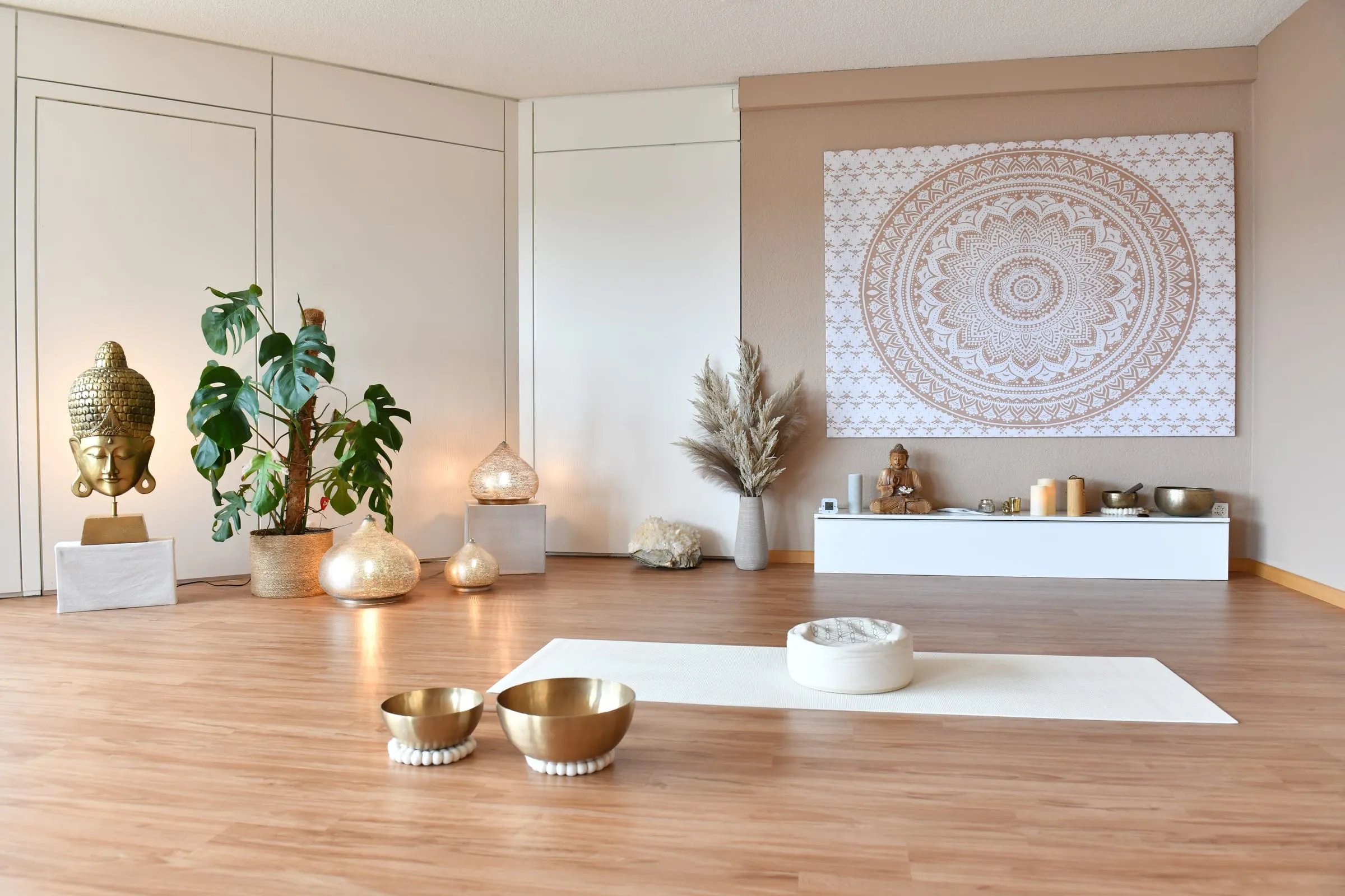 Heller Yogaraum mit einer Matte, Klangschalen und einem Mandala an der Wand